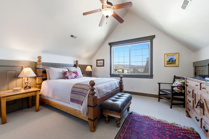 Vaulted ceiling with a ceiling fan, carpet flooring, a large window with gridded panes, wood paneling, and a wood-finish dresser