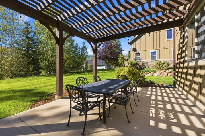 Expansive concrete patio featuring a wood pergola and a grassy backyard with mature trees