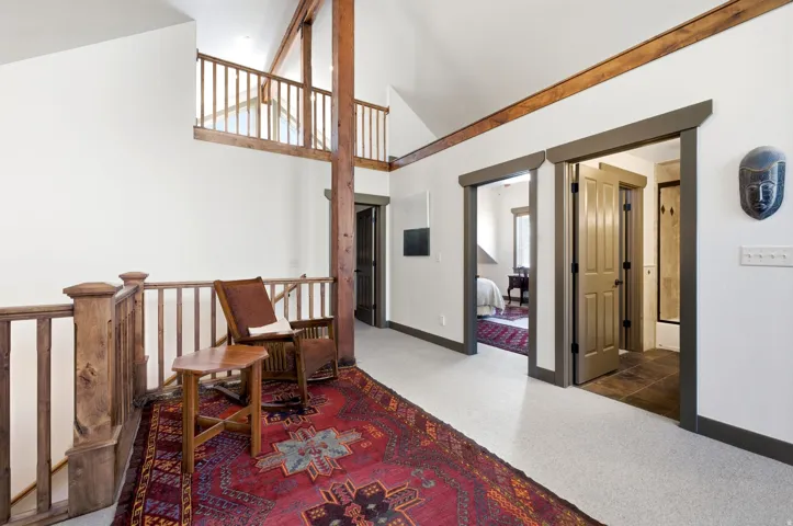Vaulted ceiling featuring exposed wood beams, wood-finish railing, and light-colored flooring