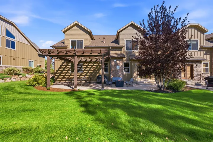 Expansive green lawn with mature landscaping, a stone patio, and a wood pergola