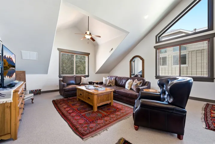Vaulted ceiling with ceiling fan, wood-frame windows, and carpet flooring