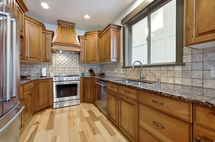 Kitchen featuring wood-finish cabinetry, stainless steel appliances, speckled countertops, tile backsplash, and wood-finish flooring
