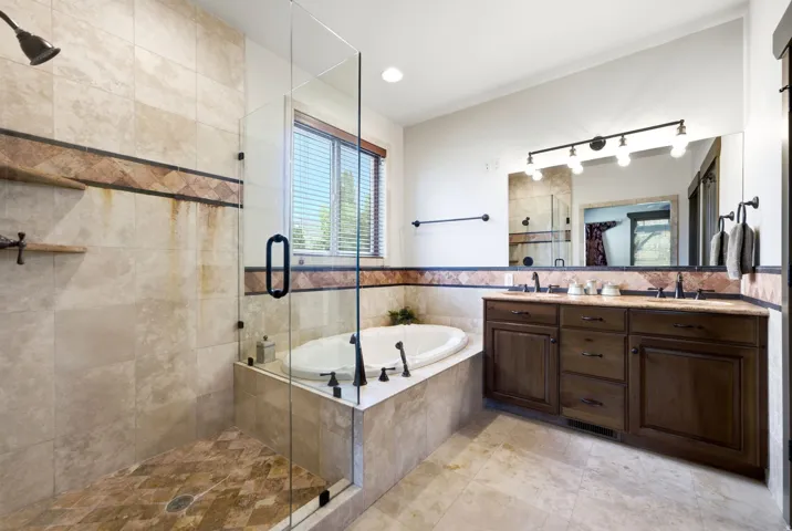 Glass-enclosed shower with tiled walls and floor, built-in corner tub, and a double vanity with wood cabinetry and a large mirror