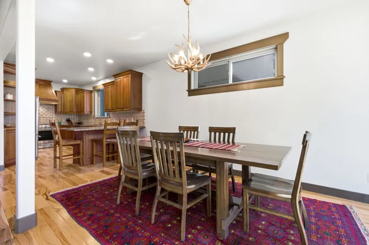 Open-concept dining area with wood-finish flooring, a unique antler-style chandelier, and a kitchen featuring wood cabinetry, a tile backsplash, and recessed lighting
