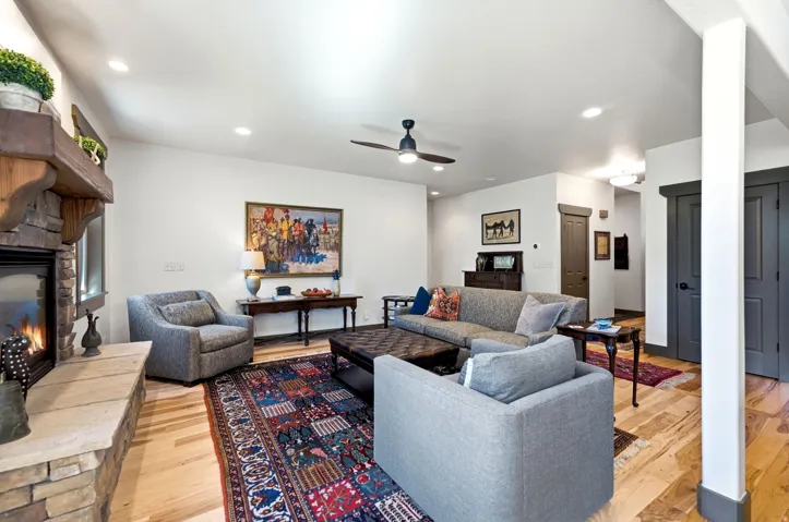 Stone-clad fireplace with wood mantel, recessed ceiling lights, wood-finish flooring, and a ceiling fan