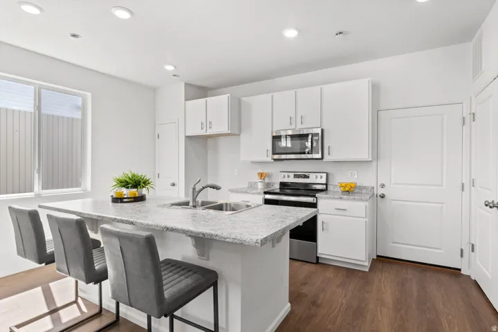 Kitchen featuring a large island with stone-finish countertop, white cabinetry, stainless steel appliances, and wood-finish flooring