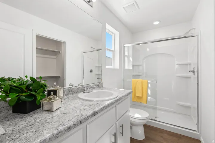 Bathroom featuring a single vanity with a light-toned countertop, an integrated sink, a glass-enclosed shower, and wood-finish flooring