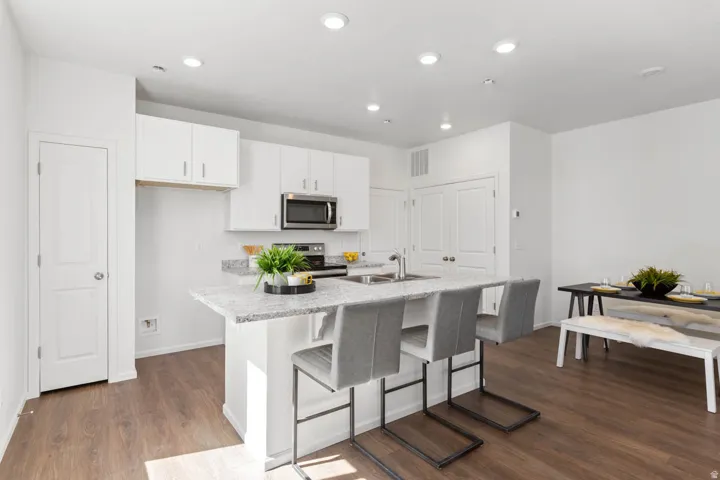 Kitchen featuring wood-finish flooring, white cabinetry, a kitchen island with a built-in sink, and stainless steel appliances