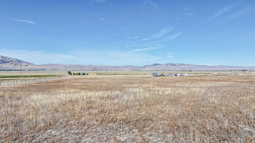 Expansive open land featuring distant mountains, a clear sky, and a distant field
