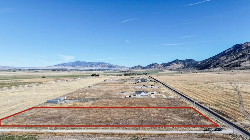 Expansive land parcel with surrounding agricultural fields, adjacent paved road, and distant mountain scenery
