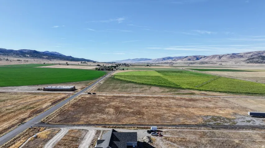 Expansive rural landscape featuring a paved road, agricultural fields, distant mountains, and a clear sky