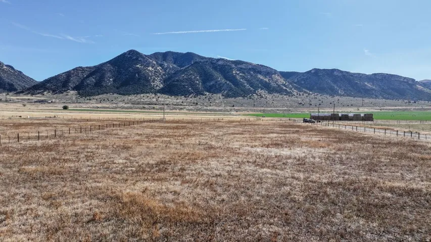 Expansive open land with a distinct mountain backdrop, featuring a partial fence line and distant green fields
