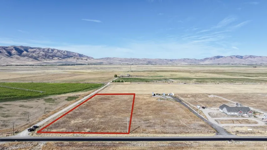 Expansive vacant land parcel, bordered by a paved road, with a distant mountain range backdrop