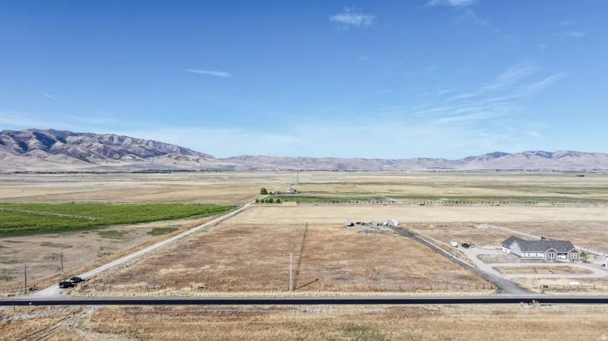 Expansive land parcel featuring open fields, distant mountain range, and a partial paved road