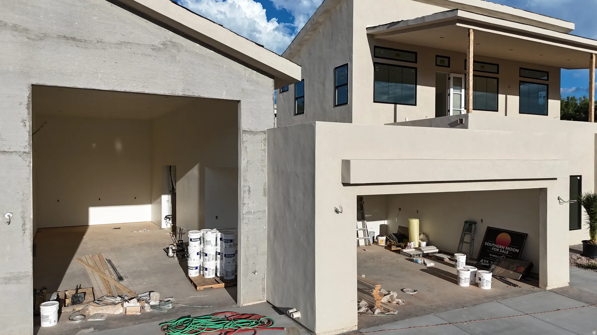Stucco exterior with multiple garage bays, covered balcony with support columns, and dark-framed windows