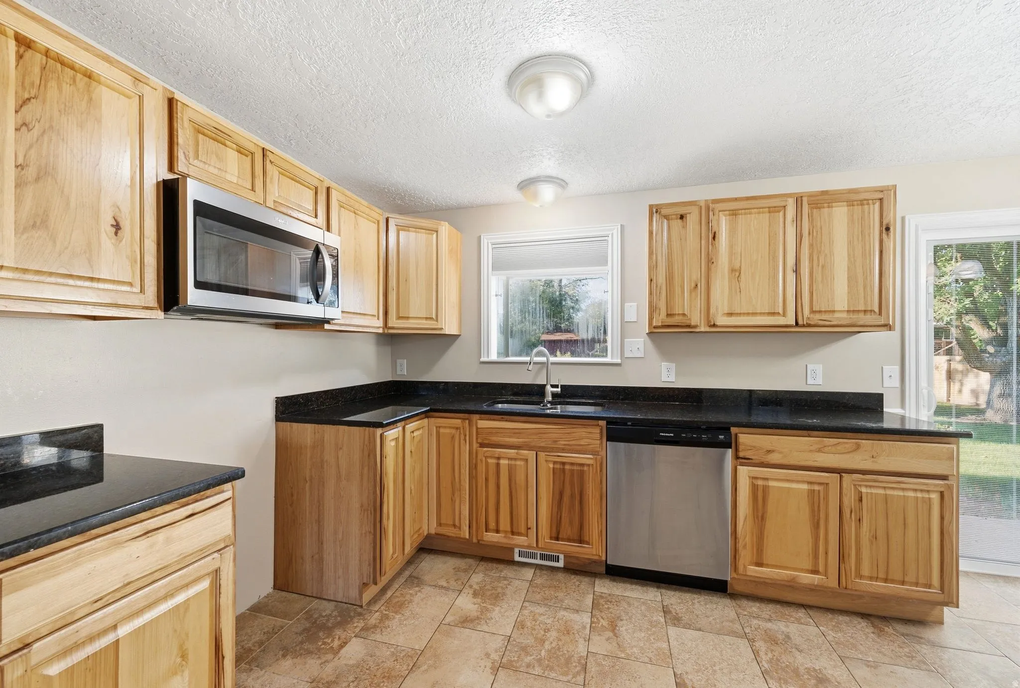 Wood cabinetry with black countertops, stainless steel microwave, stainless steel dishwasher, and a sliding glass door