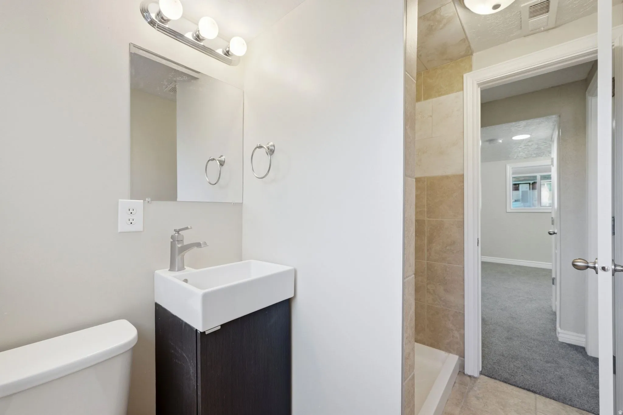 Rectangular vessel sink with a dark wood-finish vanity, brushed nickel faucet, and overhead vanity lighting