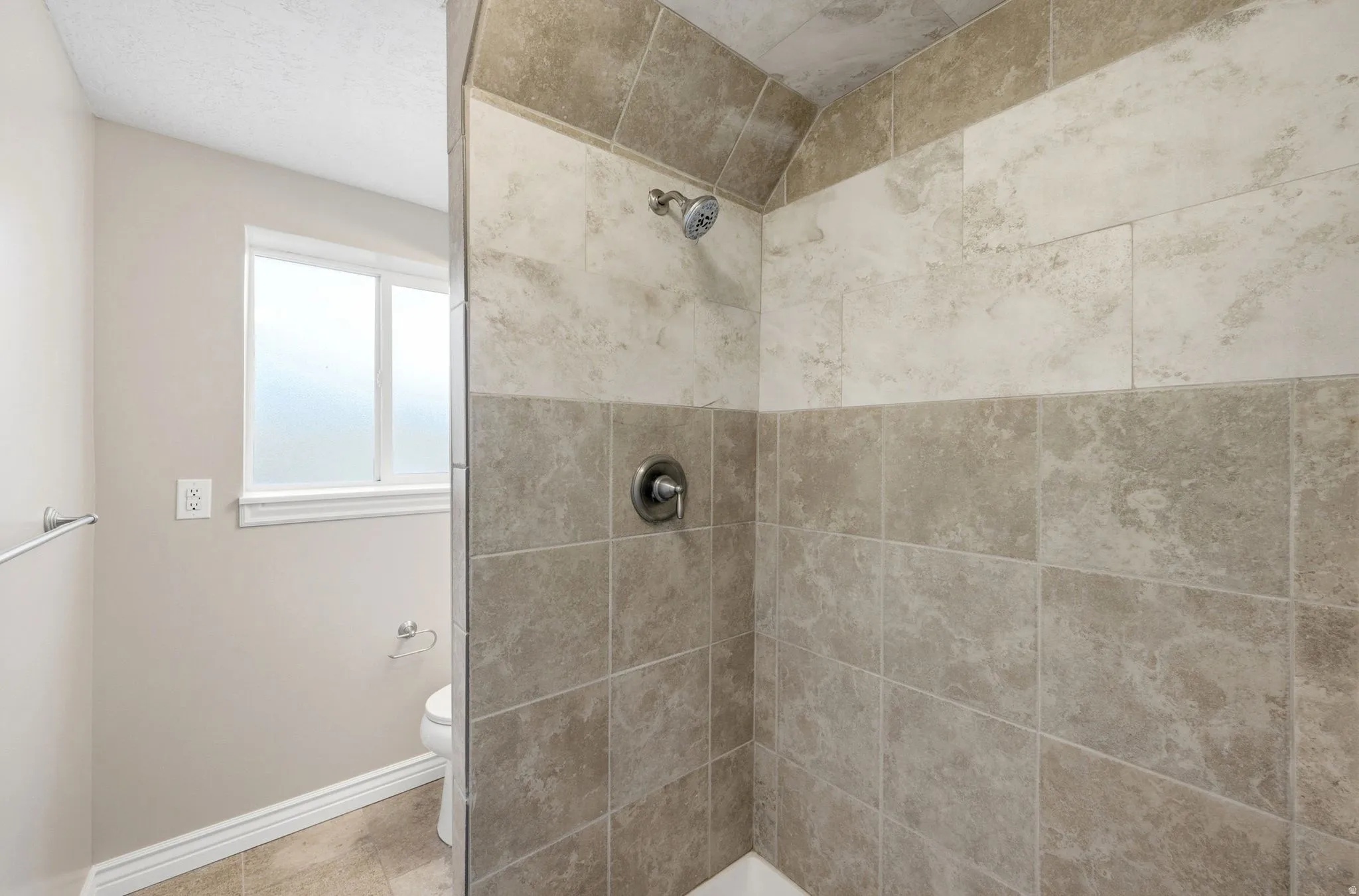 Tiled shower enclosure featuring a dual-tone wall design and a chrome shower head with a single handle control