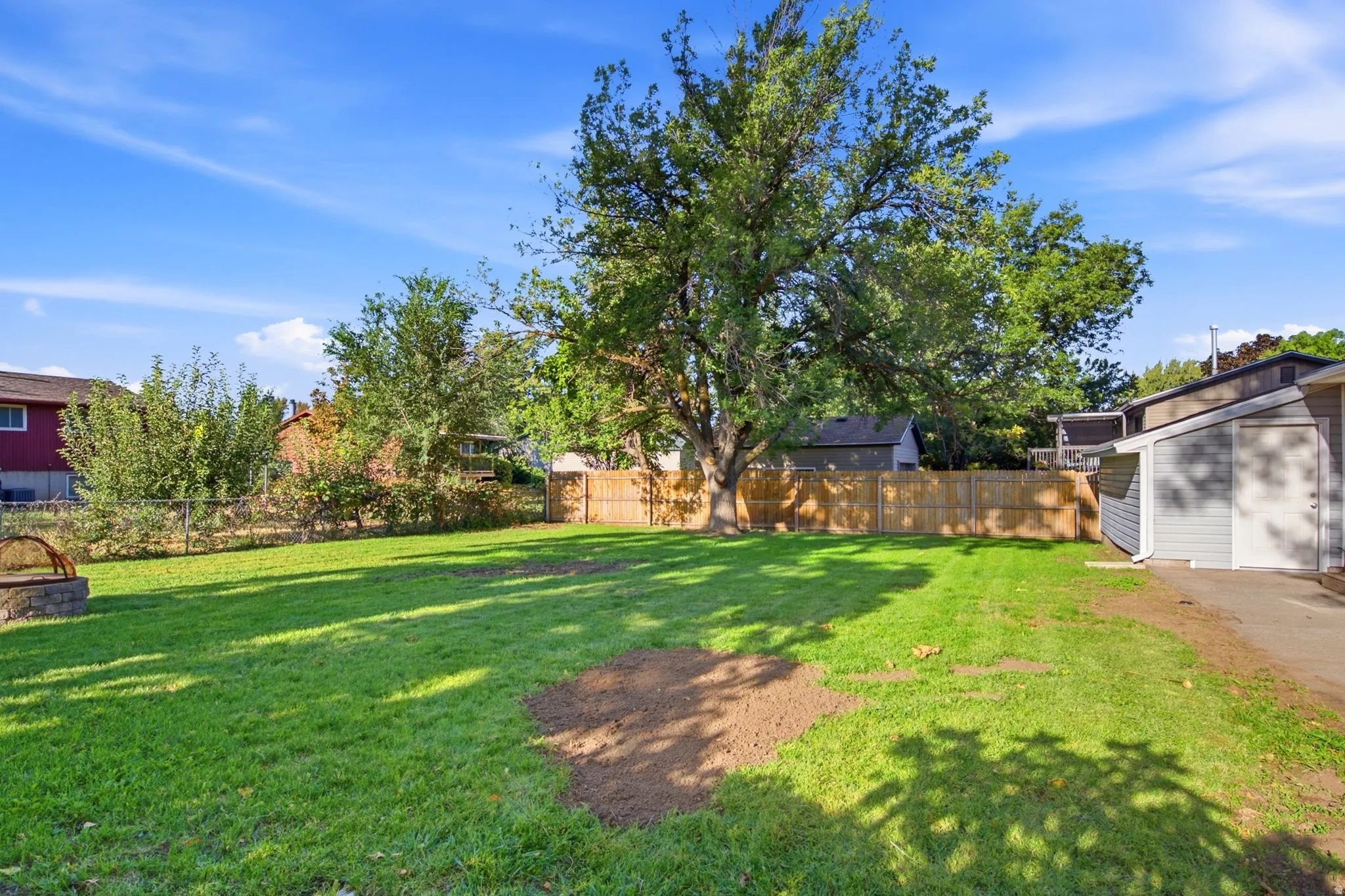 Expansive green lawn with a mature shade tree, privacy fencing, and a stone-built fire pit