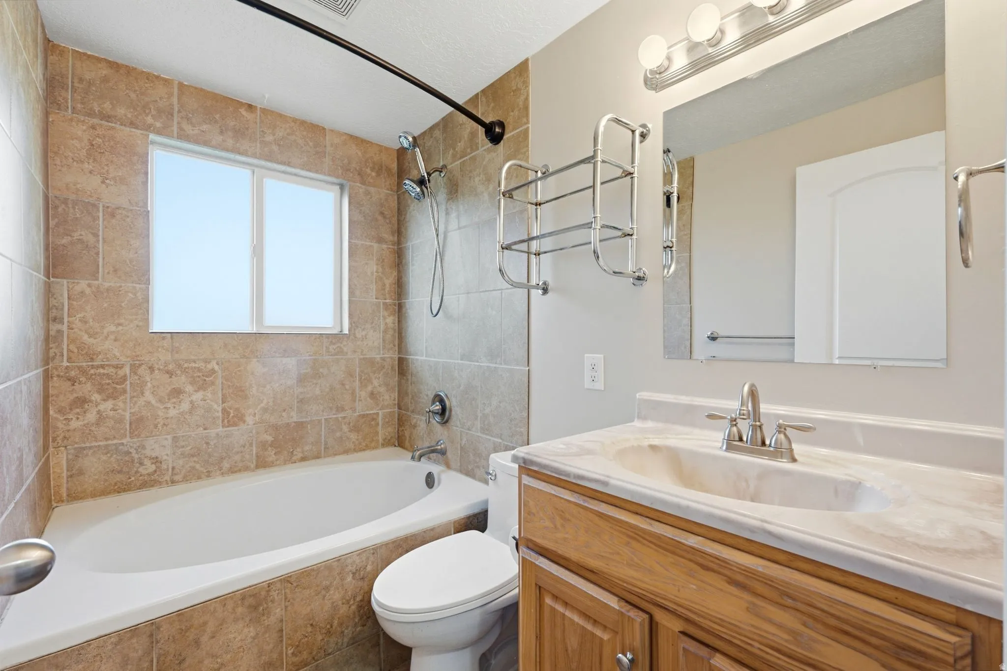 Full-tile shower and tub surround, wood-finish vanity, integrated sink, and wall-mounted mirror with overhead lighting