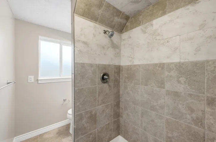 Tiled shower enclosure featuring a dual-tone wall design and a chrome shower head with a single handle control