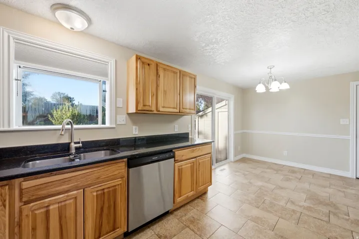 Kitchen with wood cabinetry, dark countertops, stainless steel sink, and a stainless steel dishwasher