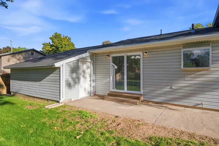 Exterior siding in light gray, featuring a sliding glass door, concrete patio, and an attached storage shed