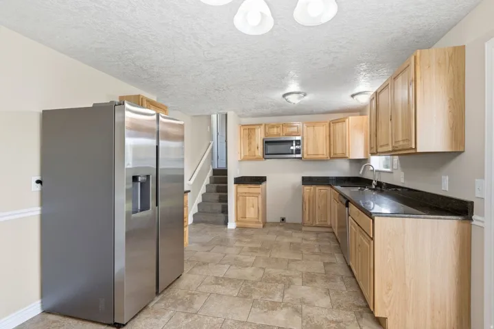 Stainless steel refrigerator, wood-finish cabinetry, dark countertops, built-in microwave, and tile flooring