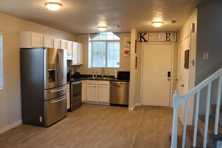 Stainless steel appliances, white cabinetry, dark countertops, wood-finish flooring, and a window above the sink