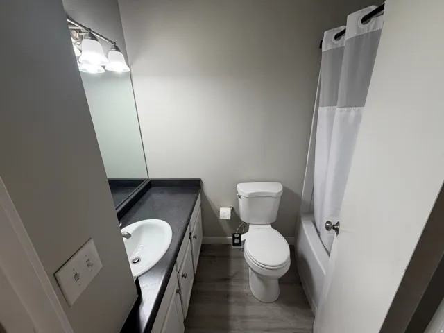 Compact bathroom featuring a white ceramic pedestal sink with chrome fixtures, a white porcelain toilet, wood-finish flooring, and a translucent shower enclosure with chrome hardware