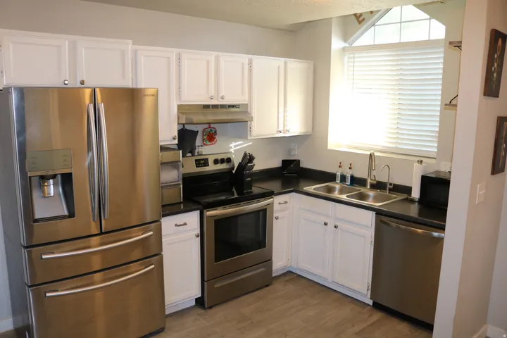 Stainless steel appliances, white cabinetry, dark countertops, a double basin sink, and wood-finish flooring