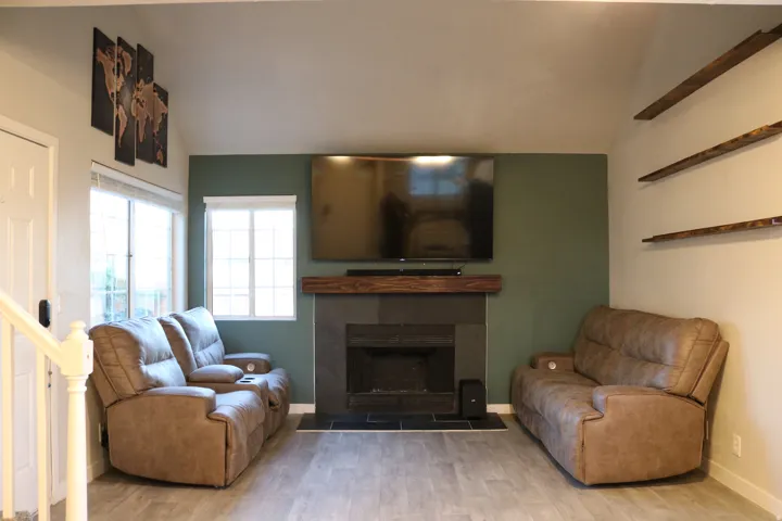 Vaulted ceiling, wood-finish flooring, fireplace with stone surround, wood mantel, and multiple windows