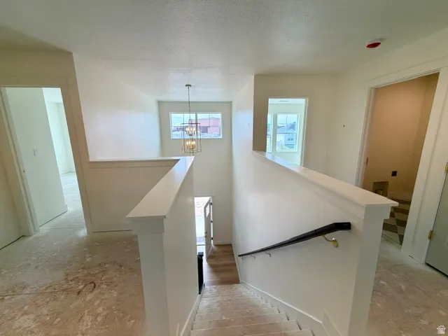 Stairway featuring a dark wood-finish handrail, white balustrade, and a suspended chandelier
