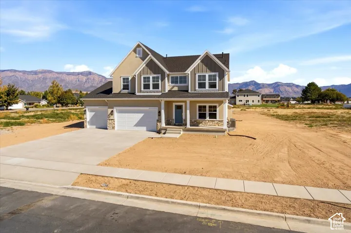 Multi-level exterior featuring a combination of stucco and vertical siding, a stone veneer foundation, a covered front porch, and a three-car garage set against a mountain backdrop