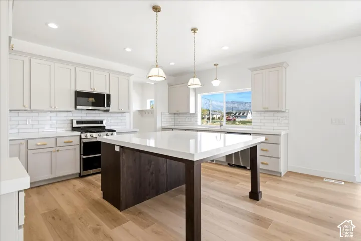 Kitchen featuring light-toned cabinetry, an island with a contrasting dark base and white countertop, white subway tile backsplash, wood-finish flooring, and recessed lighting