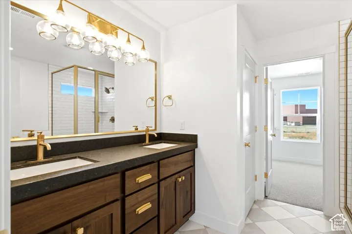 Bathroom vanity with dark wood-finish cabinetry, metallic hardware, dual drop-in sinks, and a stone-composite countertop, complemented by a gold-tone multi-bulb vanity light fixture