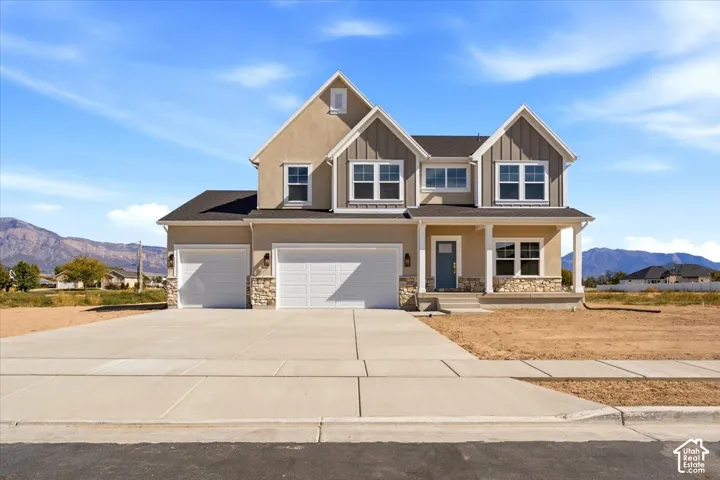 Two-story exterior featuring a mix of stucco and vertical siding, stone veneer accents, a three-car garage, a covered front porch, and a mountain backdrop