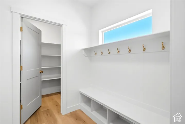 Built-in storage bench with open cubbies, wall-mounted brass hooks, overhead shelving, wood-finish flooring, and a walk-in storage area with tiered shelving