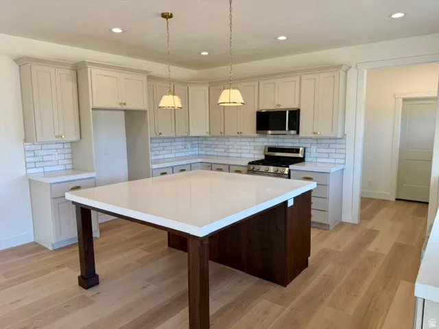 Kitchen featuring light-toned cabinetry, a large central island with a white countertop, stainless steel appliances, a white subway tile backsplash, and light wood-finish flooring