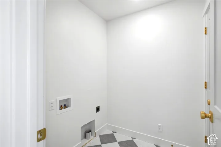 Utility space featuring recessed plumbing hookups, a dedicated vent, and geometric patterned floor tiling