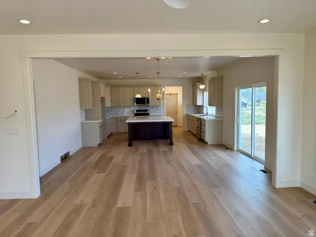 Open-concept living space with wood-finish flooring, recessed lighting, and a kitchen featuring a central island, light-toned cabinetry, and a subway tile backsplash