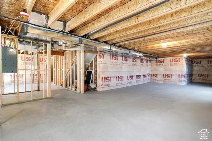 Unfinished basement featuring concrete flooring, exposed wooden ceiling joists, insulated foundation walls, and electrical panel