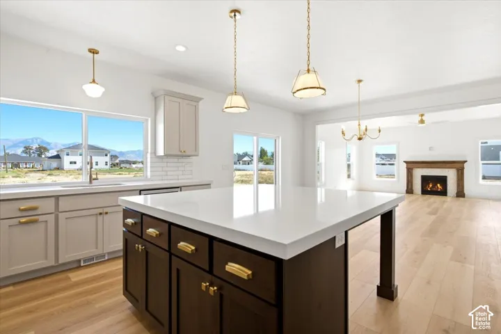 Kitchen featuring a large central island with quartz countertops, wood-finish flooring, shaker-style cabinetry with brass-tone hardware, and pendant lighting