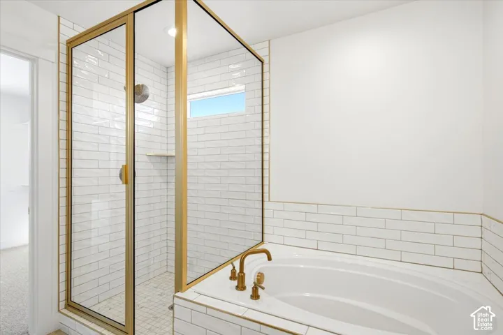 Walk-in shower with gold-finish frame, white subway tile surround, built-in corner shelf, and deep soaking tub with gold-finish hardware