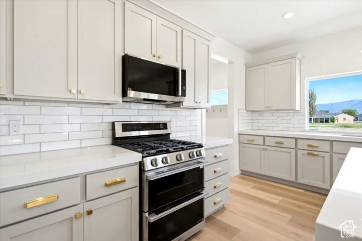 Kitchen featuring shaker-style cabinetry, quartz countertops, subway tile backsplash, stainless steel gas range, and wood-finish flooring