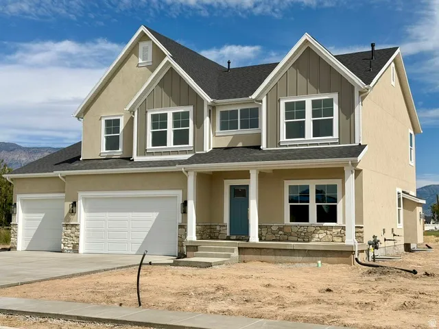 Two-story residence featuring a covered front entry, dual garage doors, stucco exterior, and stone accents