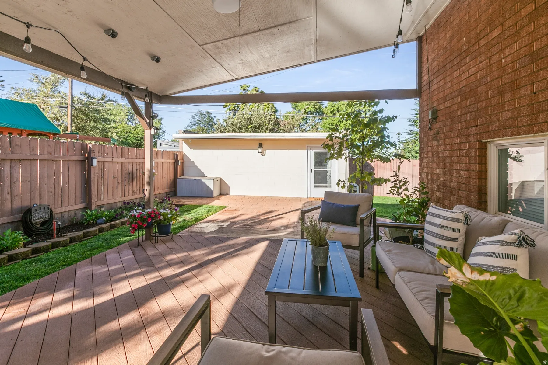 Expansive covered patio featuring wood-finish decking, string lighting, and brick exterior. Office building at the end of the patio.