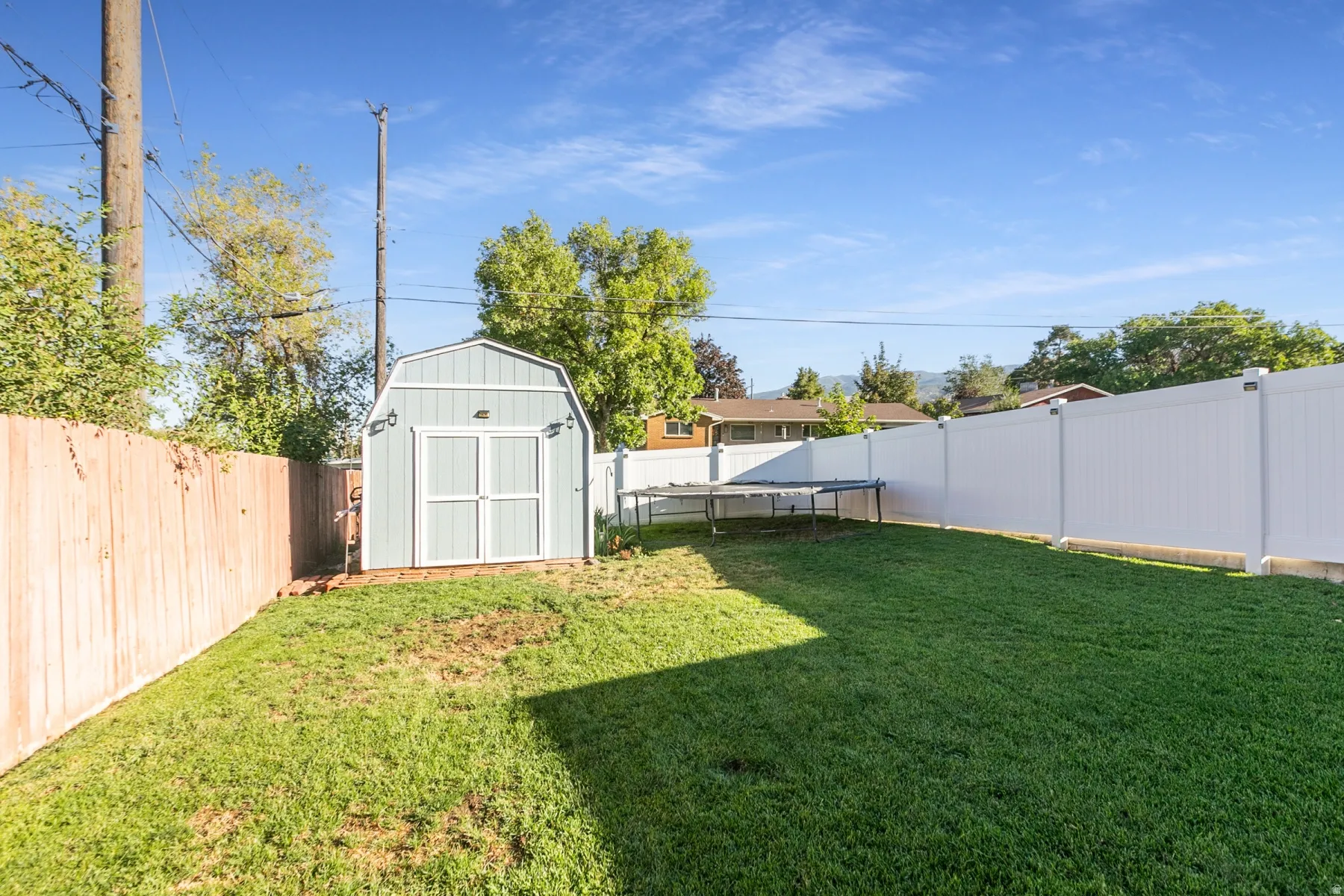 Expansive grassy yard featuring a white privacy fence, wood fence, and a storage shed with double doors