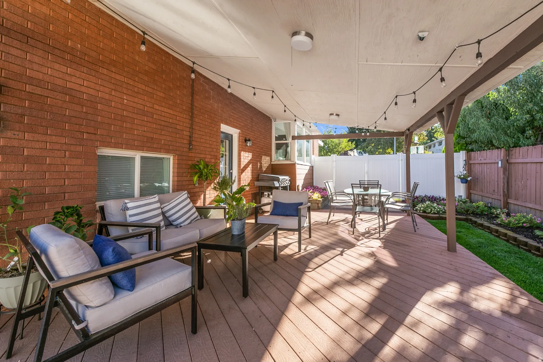 Expansive covered deck featuring a wood-finish surface, brick exterior wall, and manicured lawn