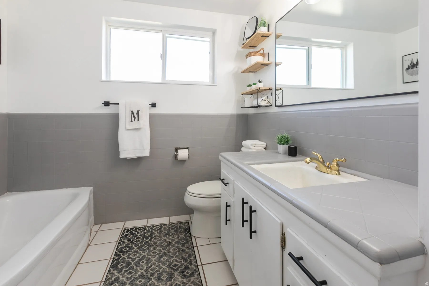 Bathroom featuring a white bathtub, toilet, vanity with integrated sink, gold-tone faucet, and a large wall-mounted mirror